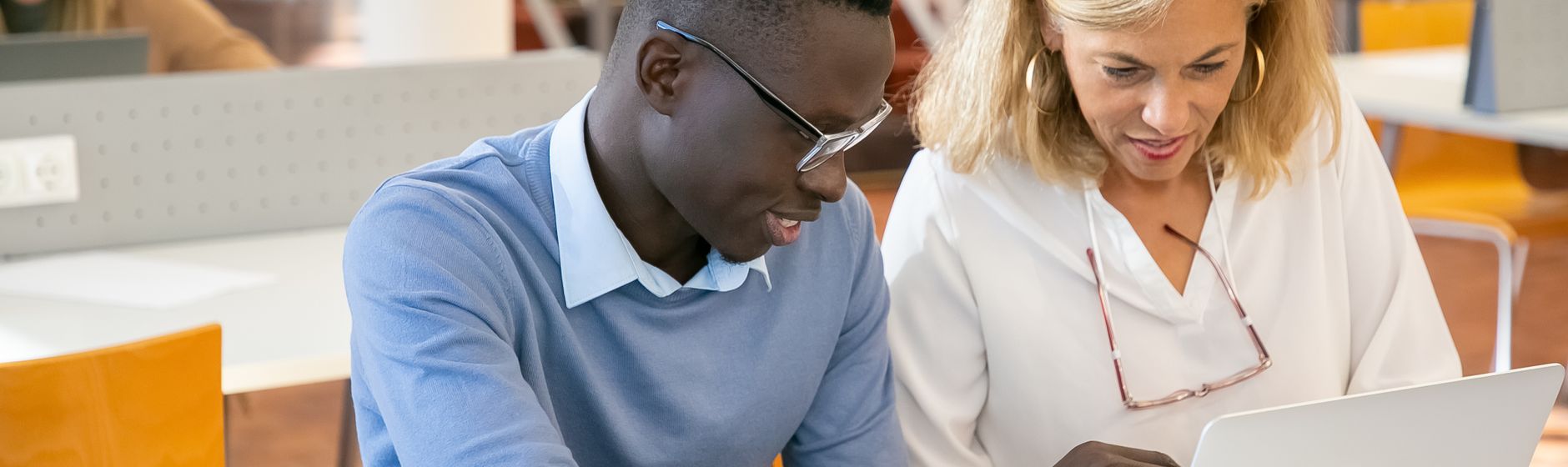 An adult student and a tutor looking together at a laptop screen in a university library
