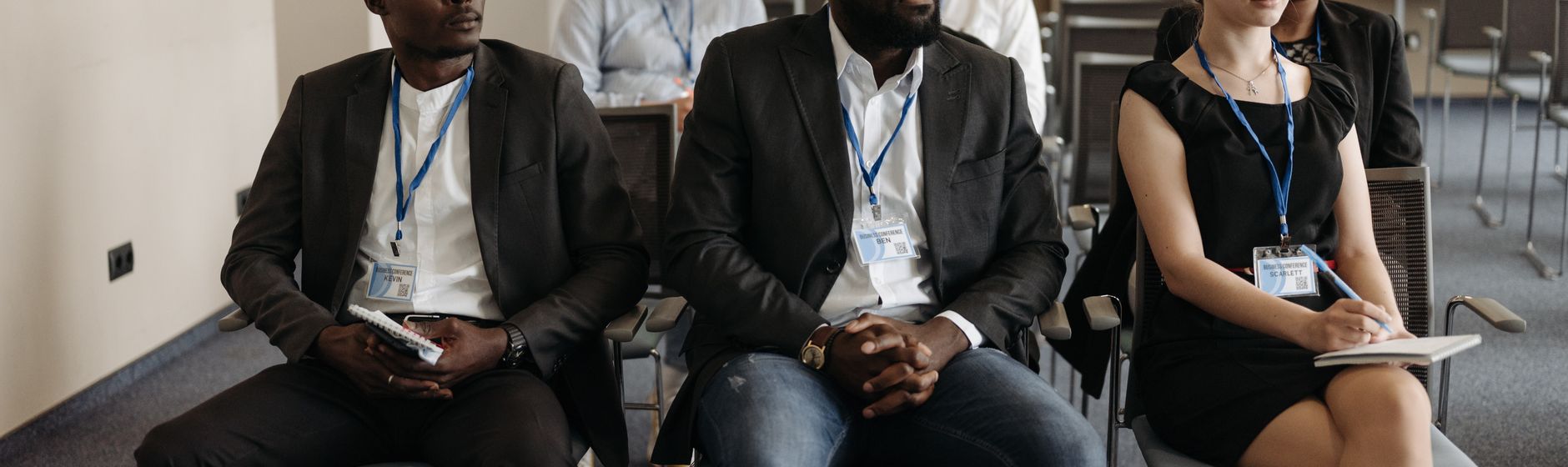 Professionals with conference badges taking notes during a seminar session, the audience a business continuity credential is built for