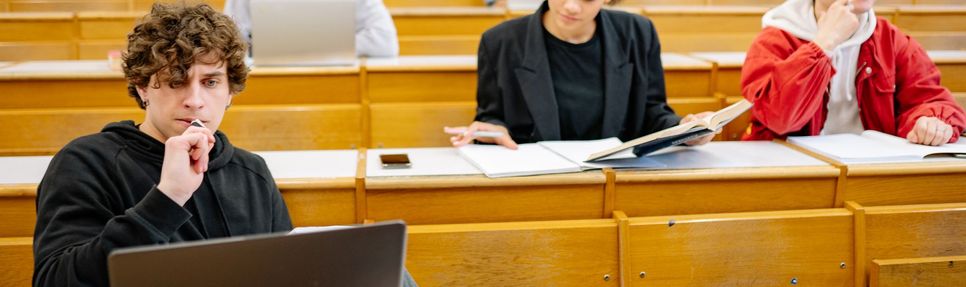 Students working with laptops and open books at the tiered desks of a university lecture hall