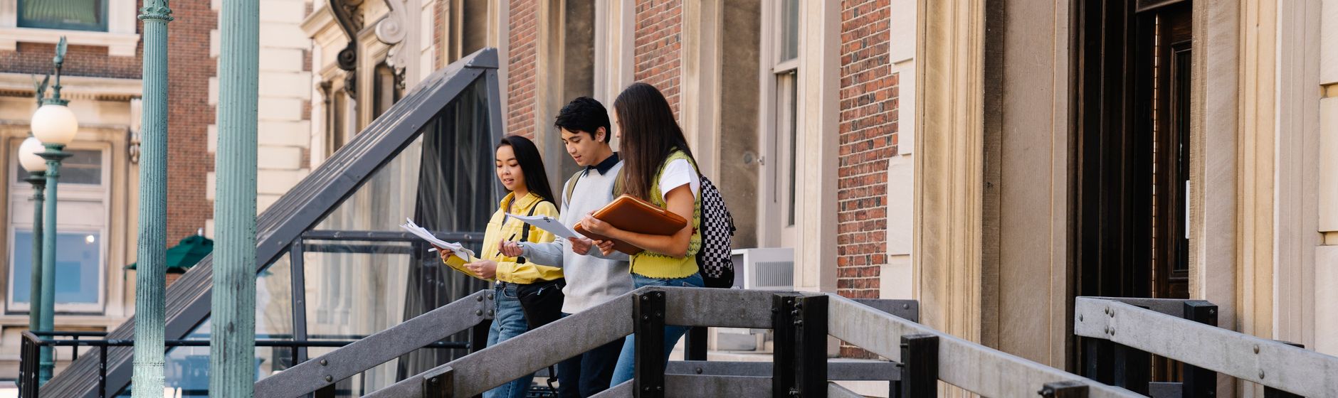 Three students reading handouts as they leave a university building together